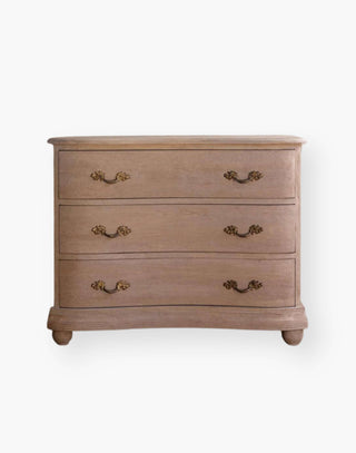 Chest of drawers made of wood with a natural finish and a subtly curved facade with French-style hardware.