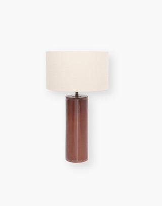 Table lamp with a tobacco full grain leather that covers the round column with a linen drum shade.