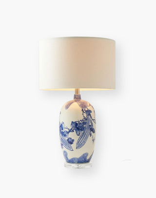 Table lamp with wild florals and prickly cucumbers hand-painted in blue gloss over a whitegloss ceramic urn. A clear resin base underlines its modernity. White linen drum shade included.