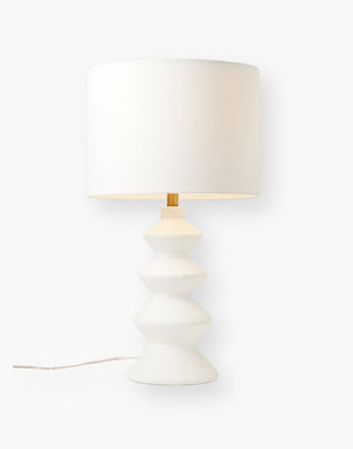 Modern table lamp with a textured matte white resin base with four undulating sections, descending in width towards the linen shade.