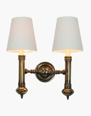 Elegant Carlton Twin Wall Sconce in cast brass with classic period design, featuring two light fixtures with ivory or black lampshades for balanced, warm illumination in vintage-inspired decor.