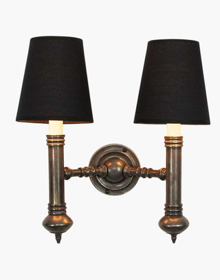 Elegant Carlton Twin Wall Sconce in cast brass with classic period design, featuring two light fixtures with ivory or black lampshades for balanced, warm illumination in vintage-inspired decor.