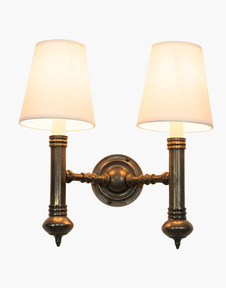 Elegant Carlton Twin Wall Sconce in cast brass with classic period design, featuring two light fixtures with ivory or black lampshades for balanced, warm illumination in vintage-inspired decor.