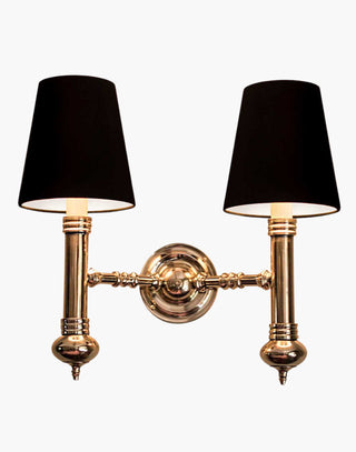 Elegant Carlton Twin Wall Sconce in cast brass with classic period design, featuring two light fixtures with ivory or black lampshades for balanced, warm illumination in vintage-inspired decor.