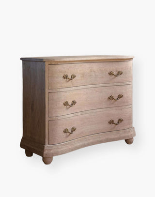 Chest of drawers made of wood with a natural finish and a subtly curved facade with French-style hardware.