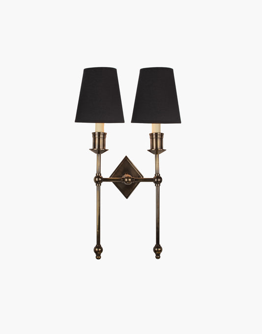 Wall sconce in cast and machined brass with diamond-shaped scalloped backplate and twin candle arms.