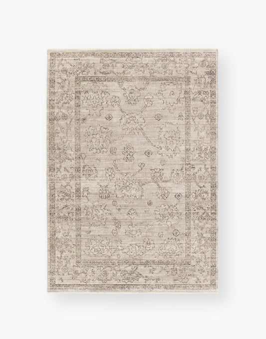 Polyester area rug that features a distressed, floral design in warm tones of brown, gray, taupe, and cream.