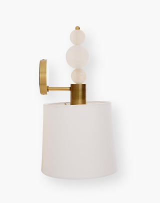 Single light sconce features three white spheres stacked on an etched cylinder that present a white linen shade with an oval antique brass iron backplate.