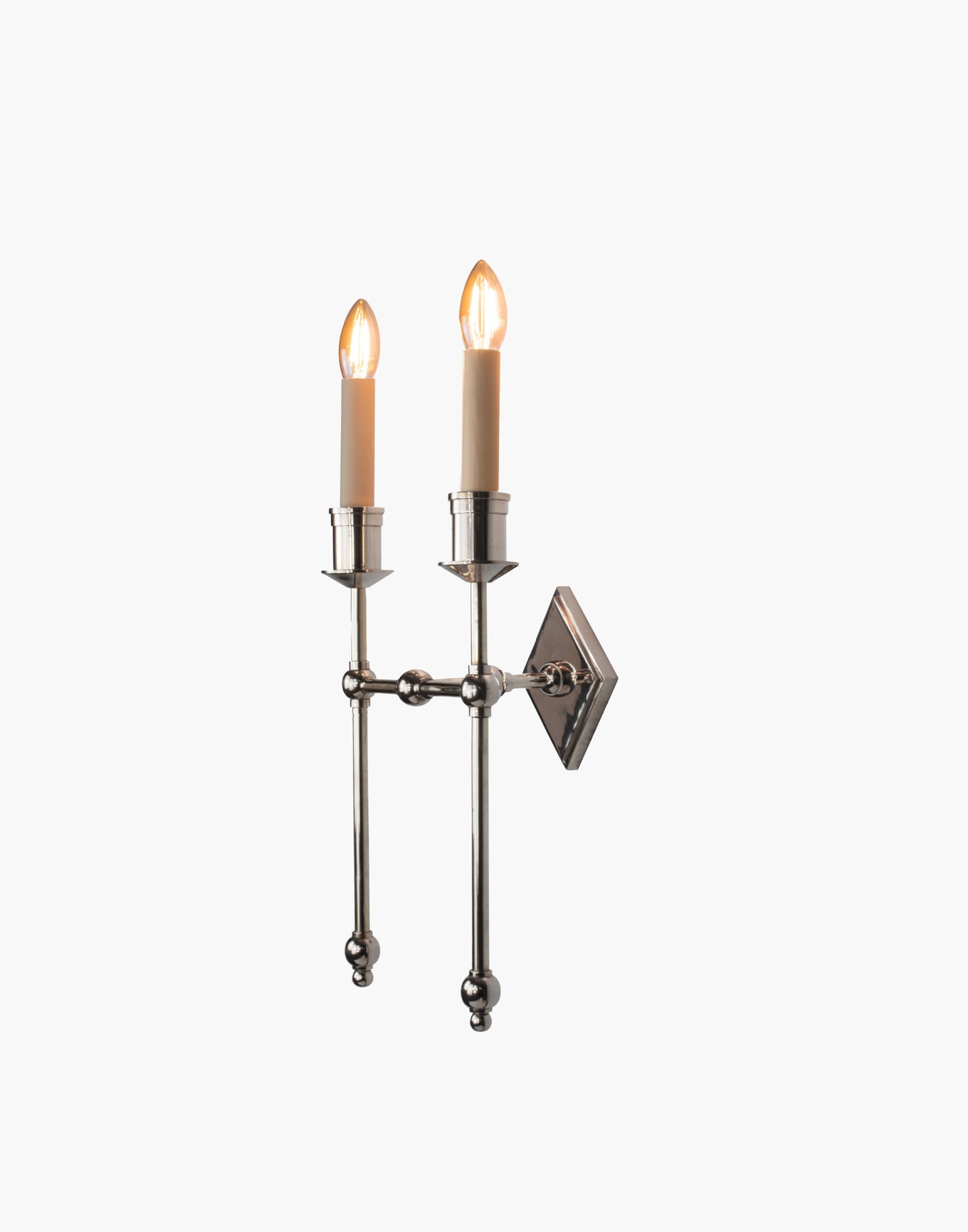 Wall sconce in cast and machined brass with diamond-shaped scalloped backplate and twin candle arms.