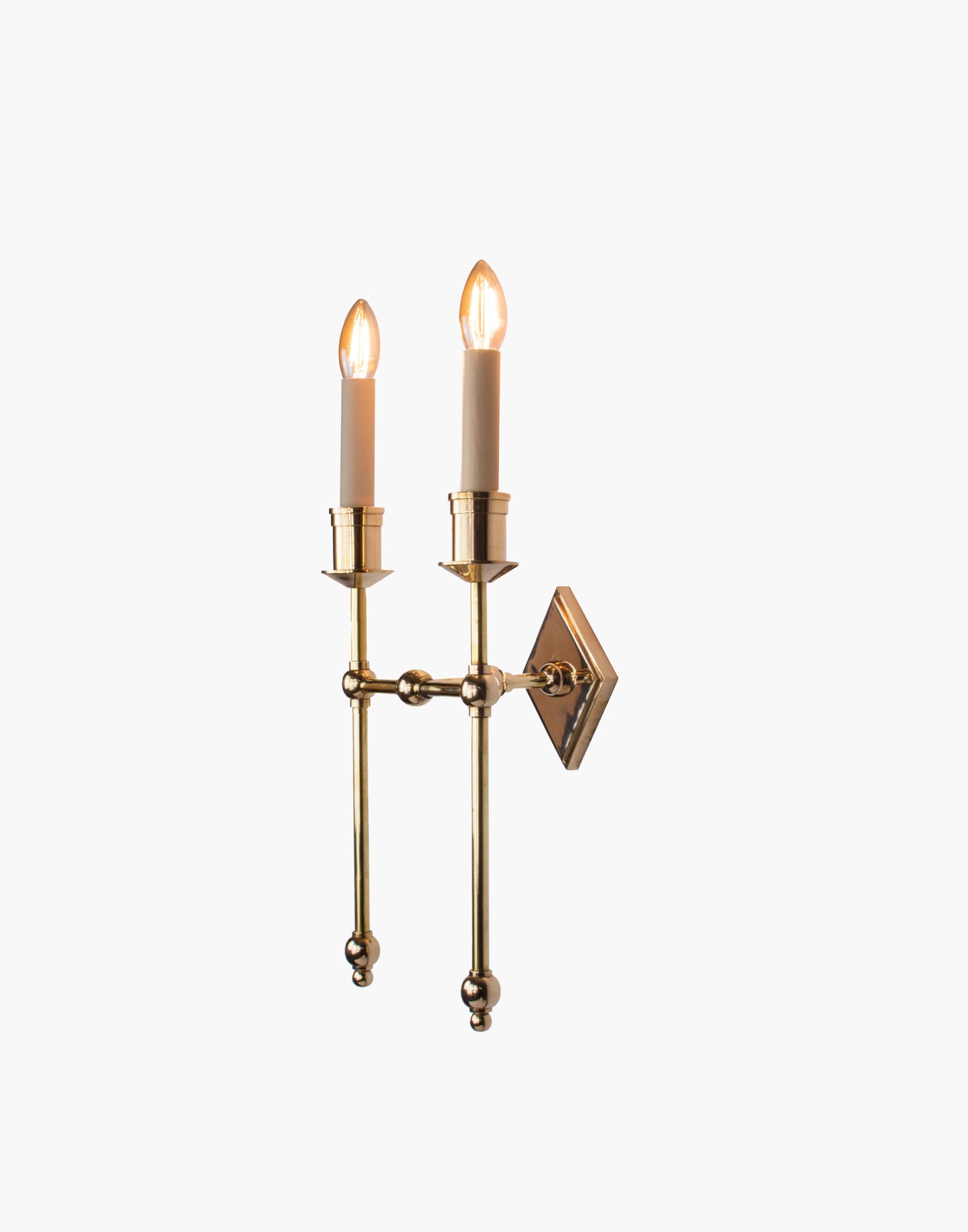 Wall sconce in cast and machined brass with diamond-shaped scalloped backplate and twin candle arms.