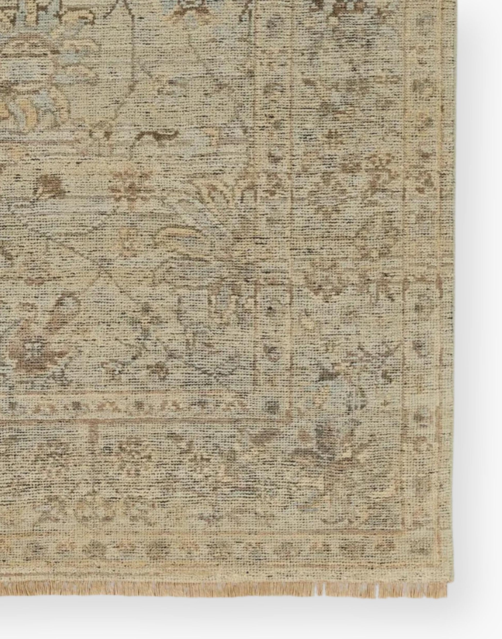 Wool area rug with a washed floral motif, decorative border, and green tones accented with tan and gray hues.