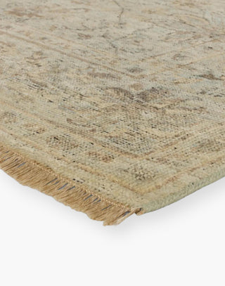 Wool area rug with a washed floral motif, decorative border, and green tones accented with tan and gray hues.