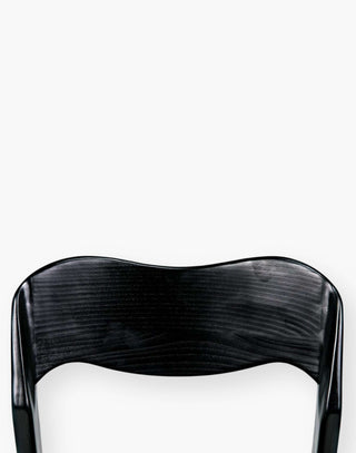 Dining chair with a subtly scalloped back and a curved seat with a black-finished sungkai wood frame.